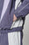 A person wears the LIVE FAST DIE YOUNG Basic Nylon Trackjacket in purple and white, with one hand in the pocket. The cropped image shows only the torso and upper legs, highlighting the color-block design, elastic cuffs, and seitliche Eingrifftaschen.