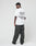A man stands facing away in the LFDY Sharkhunter Tee by LIVE FAST DIE YOUNG, an oversize white T-shirt with back text, paired with loose dark jeans and white sneakers against a plain light background.