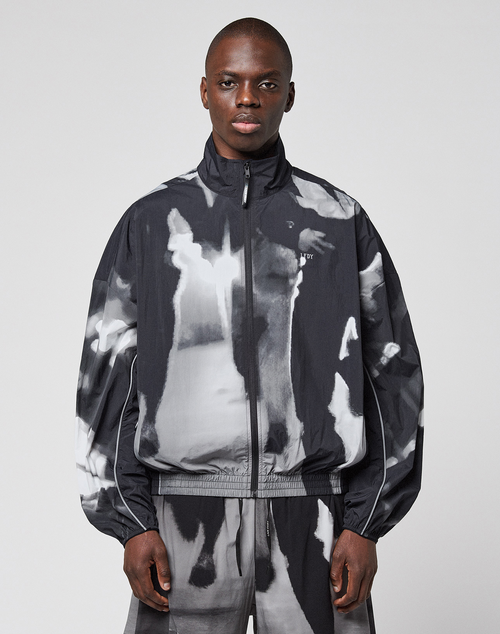 A person wearing a loose-fitting, black and white LFDY Performance Jacket by LIVE FAST DIE YOUNG with a zip-up high collar and matching pants featuring a reflective logo print stands facing forward against a plain light background.