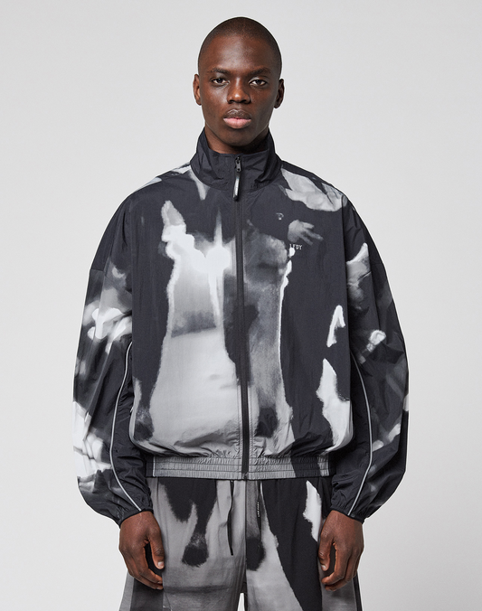 A person wearing a loose-fitting, black and white LFDY Performance Jacket by LIVE FAST DIE YOUNG with a zip-up high collar and matching pants featuring a reflective logo print stands facing forward against a plain light background.