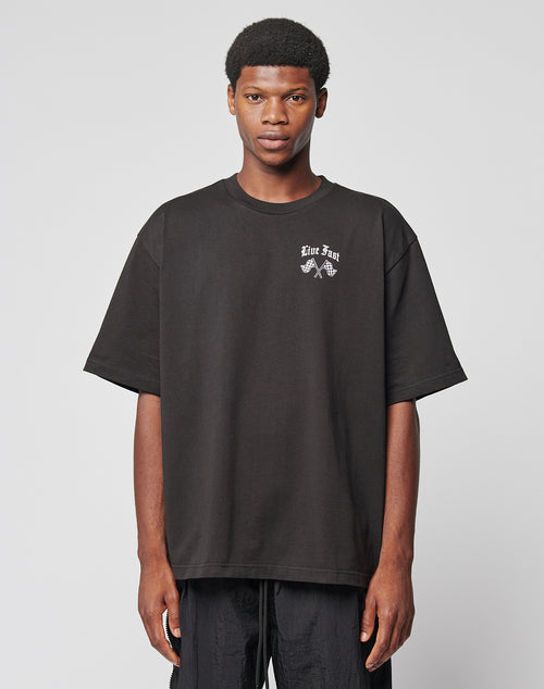 Someone wears the LFDY Haters Tee by LIVE FAST DIE YOUNG, an oversize black t-shirt with small white text and graphic prints on the chest and back, standing against a plain light gray background.