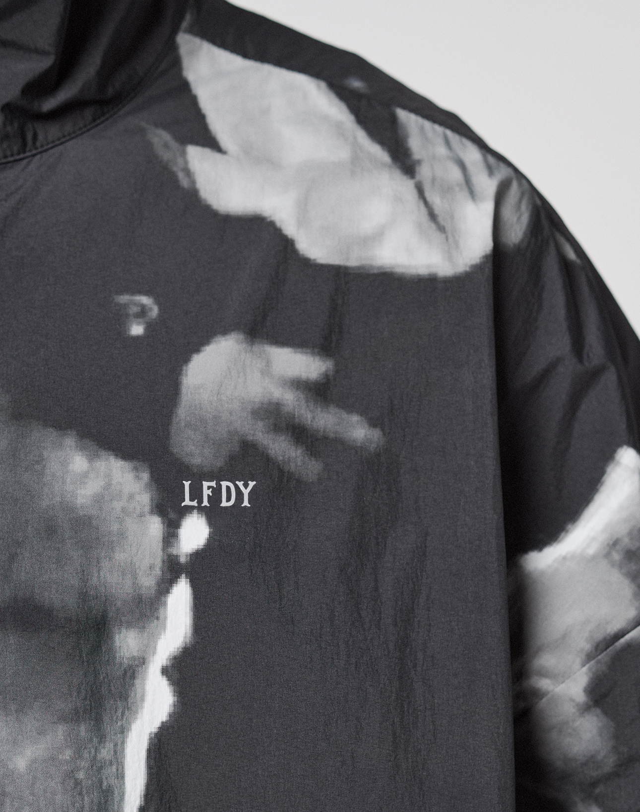 A close-up of the black LFDY Performance Jacket by LIVE FAST DIE YOUNG, featuring white "LFDY" lettering and an allover grayscale abstract print that may depict a hand.