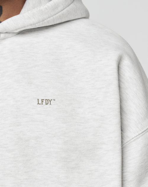 Close-up of the light gray Basic Hooded Zip by LIVE FAST DIE YOUNG with subtle distressing and small embroidered LFDY branding on the chest. Visible are part of the hood and shoulder, plus a hint of neck and chin at the top left.
