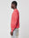 A person stands in profile against a plain background, wearing the LIVE FAST DIE YOUNG LFDY Washed Knit Sweater in coral pink with an oversize fit, paired with light-washed jeans featuring a visible back pocket.