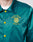 A person wearing the LIVE FAST DIE YOUNG Rhine Area College Jacket in teal nylon, featuring yellow buttons, side pockets, yellow Live Fast, Die Last, Rhine Area Family Inc. embroidery, and a circular emblem on the left chest.