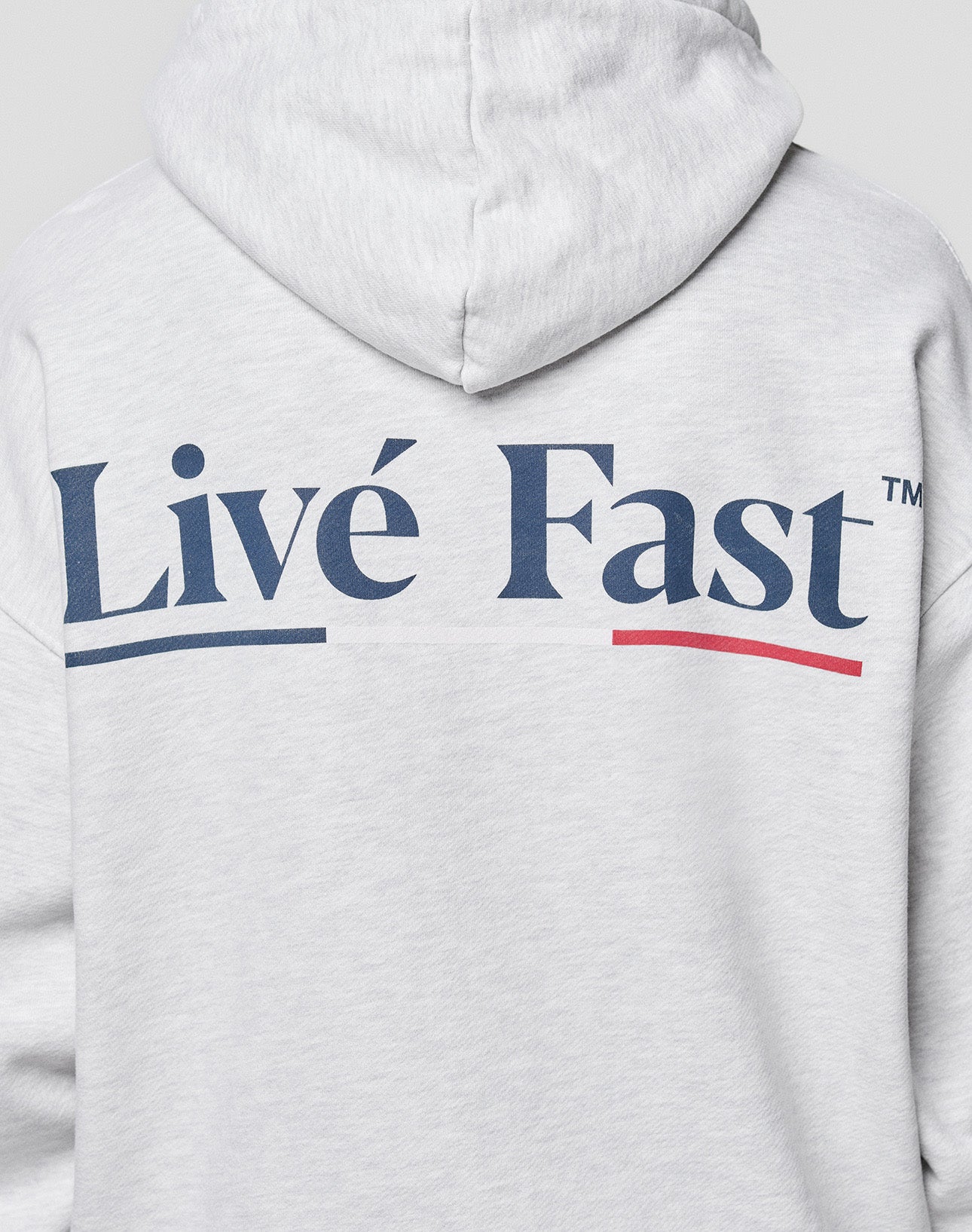 Someone wears an oversized, light gray LIVE FAST DIE YOUNG Live Fast Paris Hooded, featuring bold blue “Livé Fast™” with a red underline and accented "e" on the back, plus front and back prints.