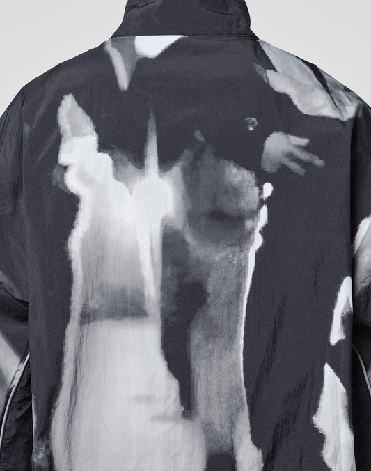The LFDY Performance Jacket by LIVE FAST DIE YOUNG features a black-and-white abstract nylon pattern with blurred shapes, a reflective logo print on the back, and delivers a modern edge.