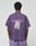 A person in a purple Basic Evidence Tee by LIVE FAST DIE YOUNG, made from 100% Baumwolle, featuring repeated “LiveFast” text and a graphic on the back. The front and back print design is shown from behind against a plain background.