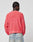 A person with braided hair wears the LFDY Washed Knit Sweater by LIVE FAST DIE YOUNG in coral-pink, featuring a subtle backprint and faint text, styled oversized. It’s 100% Baumwolle and paired with light blue, high-waisted jeans with visible back pockets.