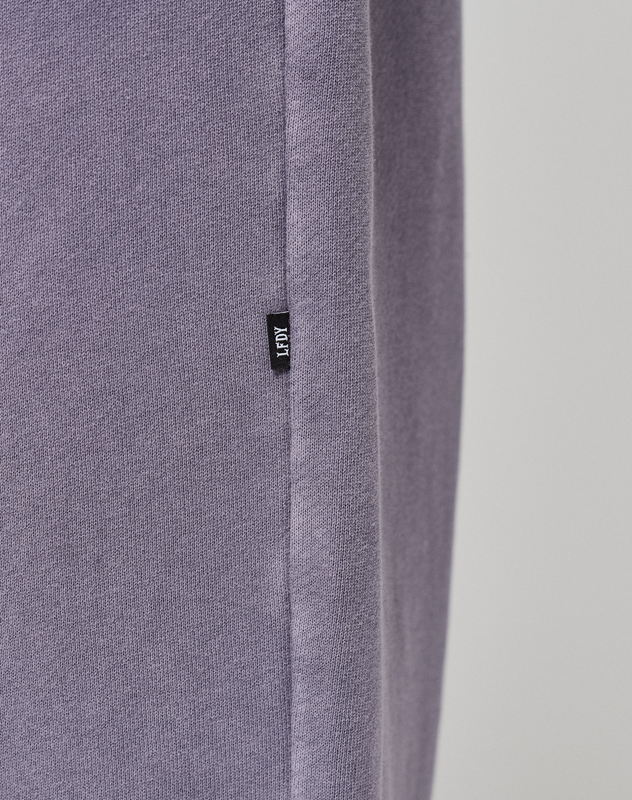 Close-up of the LFDY Hotline Loose Jogger by LIVE FAST DIE YOUNG, showing soft light purple fabric and a small black KLOT tag sewn into the seam. Features an Elastikbund for comfort against a plain, light background.