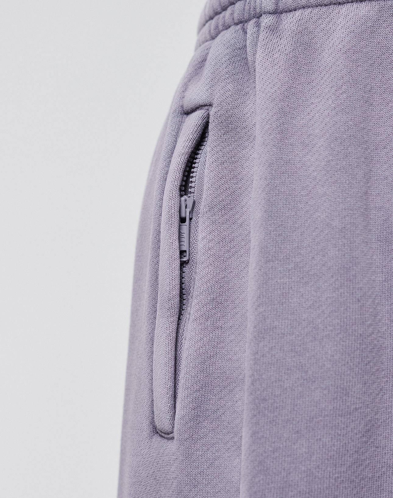 Close-up of the LFDY Hotline Loose Jogger by LIVE FAST DIE YOUNG in light purple, featuring a zippered pocket, elastic waistband, textured fabric, detailed stitching, and subtle print on the leg.