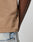 Close-up of the Live Fast Plain Tee by LIVE FAST DIE YOUNG, a beige 100% cotton T-shirt with a small black tag on the seam, paired with light blue denim jeans. Only the lower shirt, part of an arm, and jeans are visible.