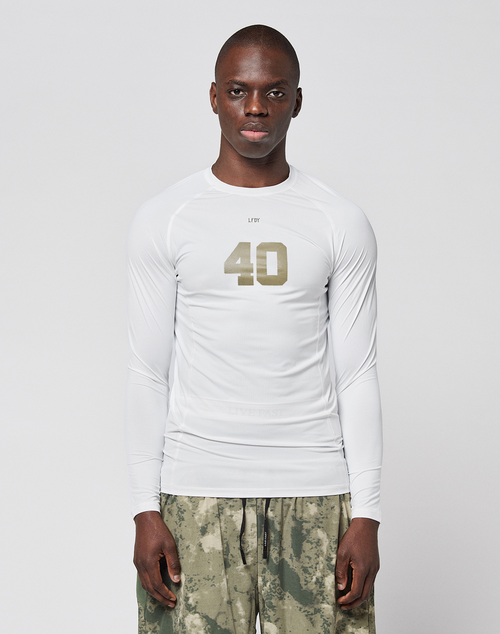 A person faces forward in a LIVE FAST DIE YOUNG LFDY Performance Slim Longsleeve, white with the number 40 on the front, and green-gray camouflage shorts made from leichtes Obermaterial, set against a plain light background.