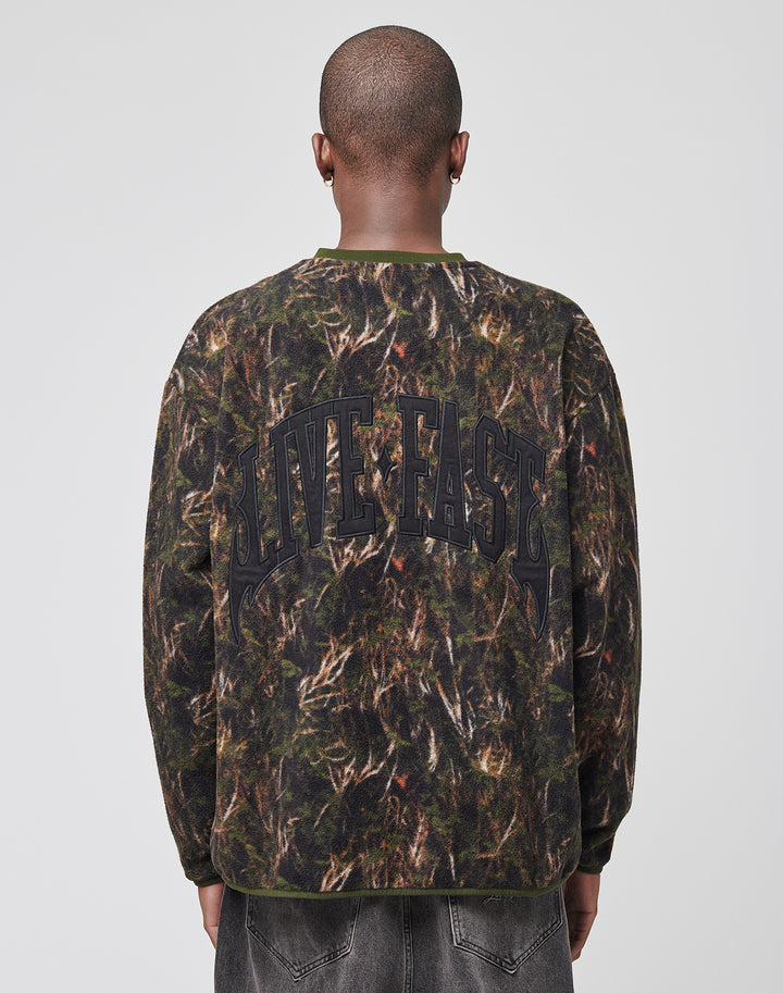 A person with a shaved head is seen from behind in an oversize LFDY Fleece Longsleeve by LIVE FAST DIE YOUNG, featuring a camouflage print and bold LIVE FAST lettering on the back. The setting is plain with a light background. | model