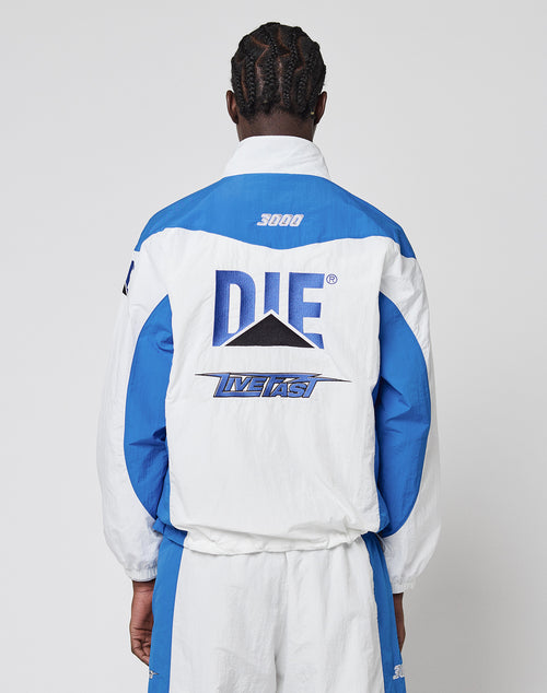 A person with braided hair, seen from behind, wears the LFDY Trackjacket 3000 by LIVE FAST DIE YOUNG. This blue and white jacket features a Multilogo Stick, bold DIE and LIVE FAST lettering, a black triangle graphic, and a Reißverschluss-Puller detail.