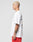 A man with short bleached blonde hair and a forearm tattoo stands in profile, wearing the LIVE FAST DIE YOUNG LFDY Haters Tee—an oversize white T-shirt with a colorful backprint—and red shorts against a plain light gray background.