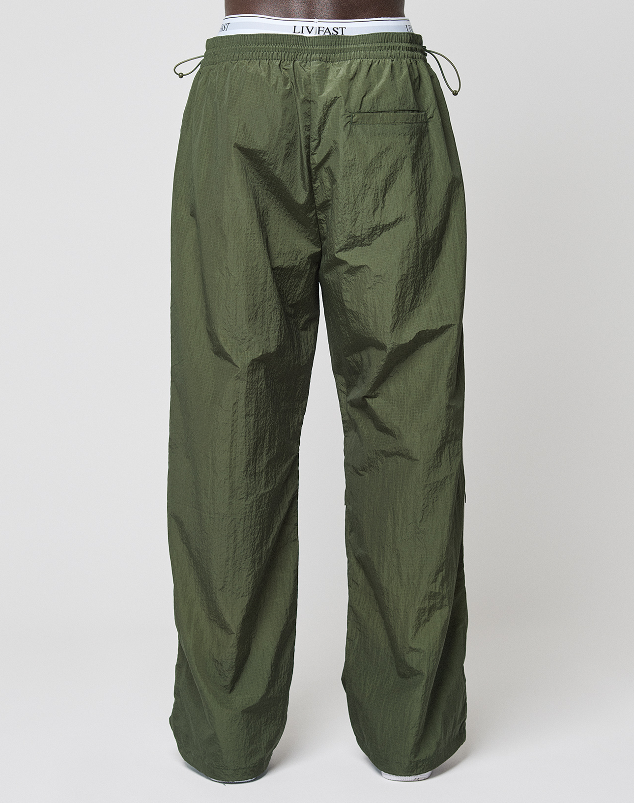 Olive green, wide fit LFDY Nylon Trackpants by LIVE FAST DIE YOUNG viewed from the back, featuring a back pocket. Worn over white elastic waistband underwear with LIVFAST logo-print branding.