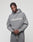 A person with braided hair wears an oversized grey LIVE FAST DIE YOUNG Basic +49 Hooded sweatshirt and matching sweatpants, featuring a bold white +49LiveFast™ frontprint. The background is plain and light-colored.