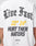 A person wears the LFDY Haters Tee by LIVE FAST DIE YOUNG—an oversized white T-shirt, crafted from soft cotton, featuring a bold black and yellow backprint: Live Fast 22 24 HURT THEM HATERS, two checkered flags, and the LFDY logo.