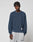 A young man with short twisted hair wears the LIVE FAST DIE YOUNG LFDY Knit Sweater in a loose, oversized blue ribbed style with light gray sweatpants, standing against a plain light gray background.