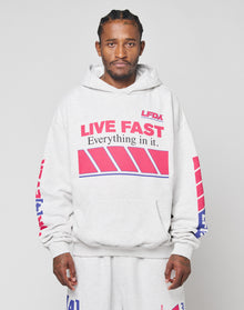 A man wears the LFDY Racing Hooded set by LIVE FAST DIE YOUNG—an oversize fit light gray hoodie and matching sweatpants with bold red and blue glossy LIVE FAST graphics—standing front-facing against a plain background. | model