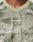 A close-up of a person wearing the LIVE FAST DIE YOUNG Camo Mesh Jersey, a light green camouflage-patterned shirt made from 100% polyester with LIVE FAST in reflective print on the chest. Only neck and upper chest are visible.
