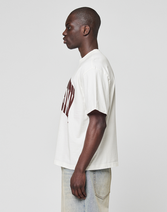 A person stands in profile facing left, wearing the LIVE FAST DIE YOUNG LFDY Block Tee—an oversize fit white T-shirt with a large red frontprint—paired with light blue jeans, set against a plain light gray background. Made from 100% Baumwolle.