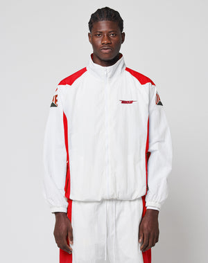 A man stands against a plain background wearing the LFDY Trackjacket 3000 by LIVE FAST DIE YOUNG, a white and red zip-up jacket with branded zipper puller, multi-logo embroidery, red accents, graphic patches, and matching regular fit track pants.