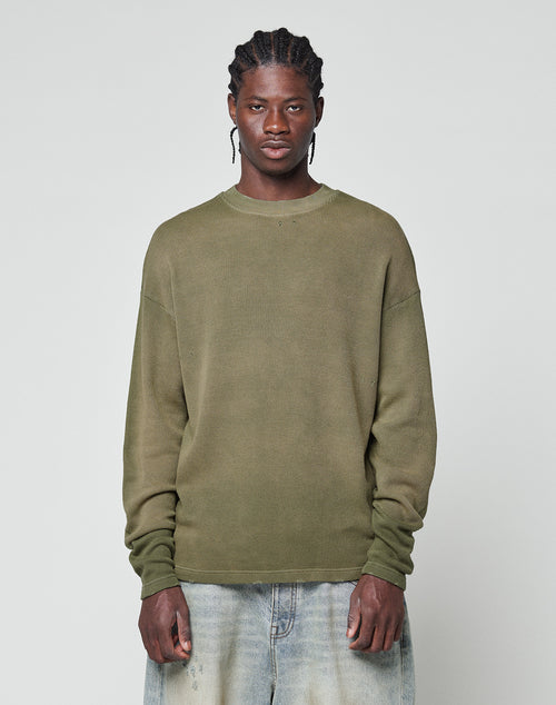 A person stands facing forward, wearing the olive LFDY Rib Knit Longsleeve by LIVE FAST DIE YOUNG and light blue jeans with a unique wash effect, set against a plain light gray background.