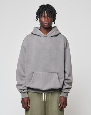 A person with short, twisted hair wears the LIVE FAST DIE YOUNG Basic Blank Hooded in oversize fit and olive green pants, standing against a plain light gray background.