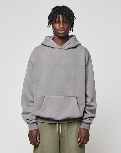 A person with short, twisted hair wears the LIVE FAST DIE YOUNG Basic Blank Hooded in oversize fit and olive green pants, standing against a plain light gray background.