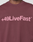A person wearing the LIVE FAST DIE YOUNG Basic +49 Tee, an oversize fit maroon shirt made from 100% Baumwolle, featuring a pink +49LiveFast™ front print across the chest.