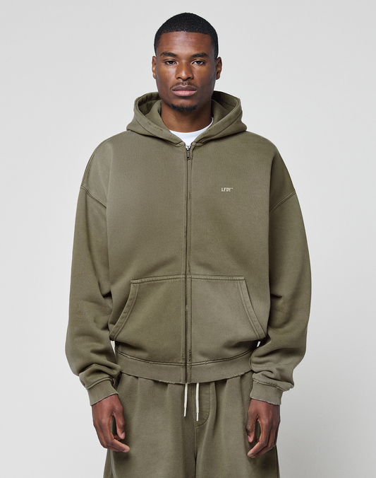 A man faces forward against a plain light background, wearing the LIVE FAST DIE YOUNG Basic Hooded Zip in olive green with a faded finish and matching sweatpants, his hands relaxed at his sides.