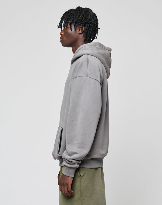 A person with short, textured hair stands sideways in a loose LIVE FAST DIE YOUNG Basic Blank Hooded hoodie and olive green pants against a plain light gray background.
