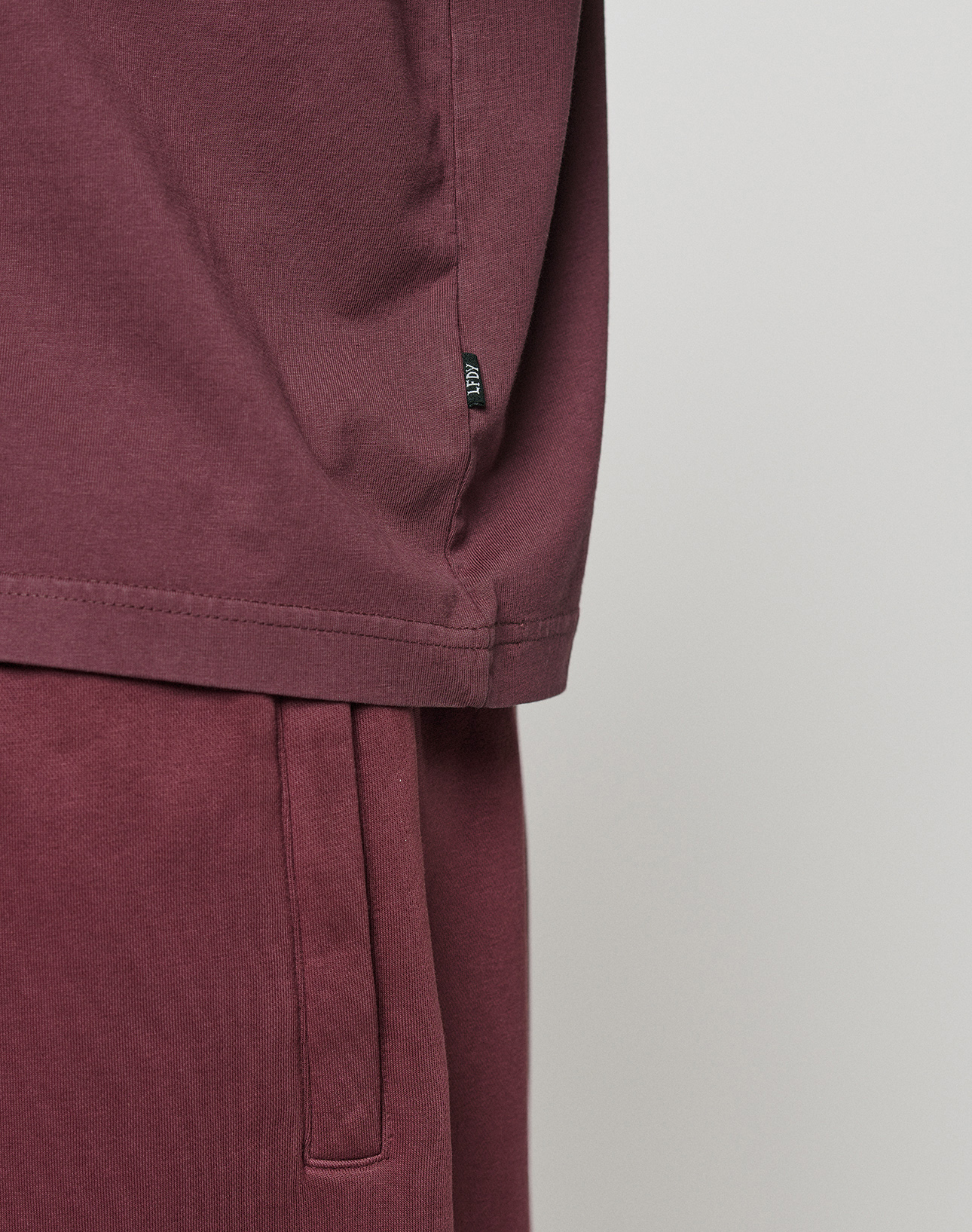 Close-up of a person in an oversize LIVE FAST DIE YOUNG Basic +49 Tee and matching sweatpants. The image highlights the soft fabric, focusing on the tee's side hem and the pants' waistband.