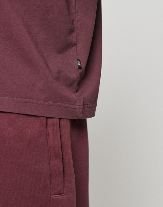 Close-up of a person in an oversize LIVE FAST DIE YOUNG Basic +49 Tee and matching sweatpants. The image highlights the soft fabric, focusing on the tee's side hem and the pants' waistband.