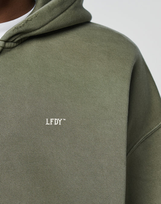 Close-up of a person wearing the olive green LIVE FAST DIE YOUNG Basic Hooded Zip, featuring white LFDY⢠embroidery on the chest and a subtly faded fabric for a casual, worn-in look.