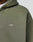 Close-up of a person wearing the olive green LIVE FAST DIE YOUNG Basic Hooded Zip, featuring white LFDY™ embroidery on the chest and a subtly faded fabric for a casual, worn-in look.