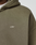 A close-up of a person wearing the LIVE FAST DIE YOUNG Basic Hooded Zip in olive green, featuring an oversize fit and white logo on the chest. A white undershirt collar is visible at the neckline.