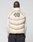 A person in the LIVE FAST DIE YOUNG Live Fast Puffer Vest—an oversized beige vest with a bold 40 and tiger graphic on the back—layered over a nylon jacket, stands facing away from the camera against a plain background.