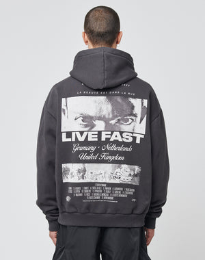 A person with short hair is seen from behind wearing the LIVE FAST DIE YOUNG LFDY Cinema Hooded in Oversize Fit, featuring a bold eye graphic, the words LIVE FAST, country names, and garment details on the back.