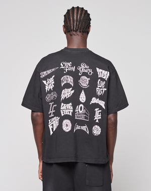 A person with braided hair is seen from behind wearing the LFDY Logo Tee by LIVE FAST DIE YOUNG, a black Oversize Fit T-shirt featuring bold white graphics and phrases like "Live Fast Die Young" on the back.