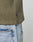 Close-up of the side of a person wearing light blue jeans and an olive green LFDY Rib Knit Longsleeve by LIVE FAST DIE YOUNG, featuring an oversized fit and a small black ADY tag near the hem against a plain, light background.