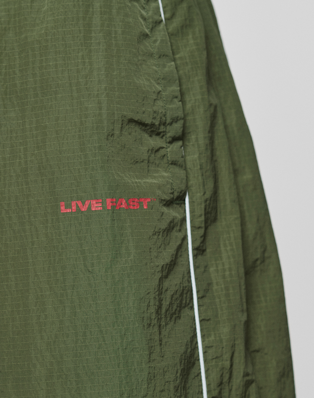 Close-up of green textured LFDY Nylon Trackshorts by LIVE FAST DIE YOUNG, in a wide fit, featuring red "LIVE FAST" lettering and a thin white vertical line on the right side.