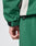 Close-up of a hand resting by the side, wearing LIVE FAST DIE YOUNG’s Basic Shell Jacket in an oversize green fit with black sleeve strap, light gray seam accent, and matching green pants.