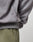Close-up of a person wearing the LIVE FAST DIE YOUNG Basic Blank Hooded in gray Baumwolle Polyester with a small black icon tag, paired with olive green pants. Focus is on the side and waist of the sweatshirt.