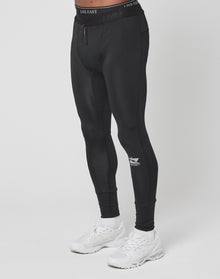 A person wearing Live Fast Performance Tights by LIVE FAST DIE YOUNG, in black slim fit with branding and elastic waistband, paired with white sneakers, stands against a plain white background. Their upper body is not visible.
