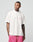 A man wearing a white LFDY Loyal Tee by LIVE FAST DIE YOUNG with an oversize fit and pink shorts stands against a plain light background, looking left with his hands in his pockets.
