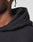 Close-up of a person with brown skin, a small gold hoop earring, and short twists wearing the LIVE FAST DIE YOUNG LFDY Script Hooded black hoodie in Oversize Fit. The background is plain and light-colored.