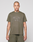 A tattooed person is wearing the LIVE FAST DIE YOUNG Live Fast Rhinestone Tee in olive green with matching shorts, standing against a plain light gray background.